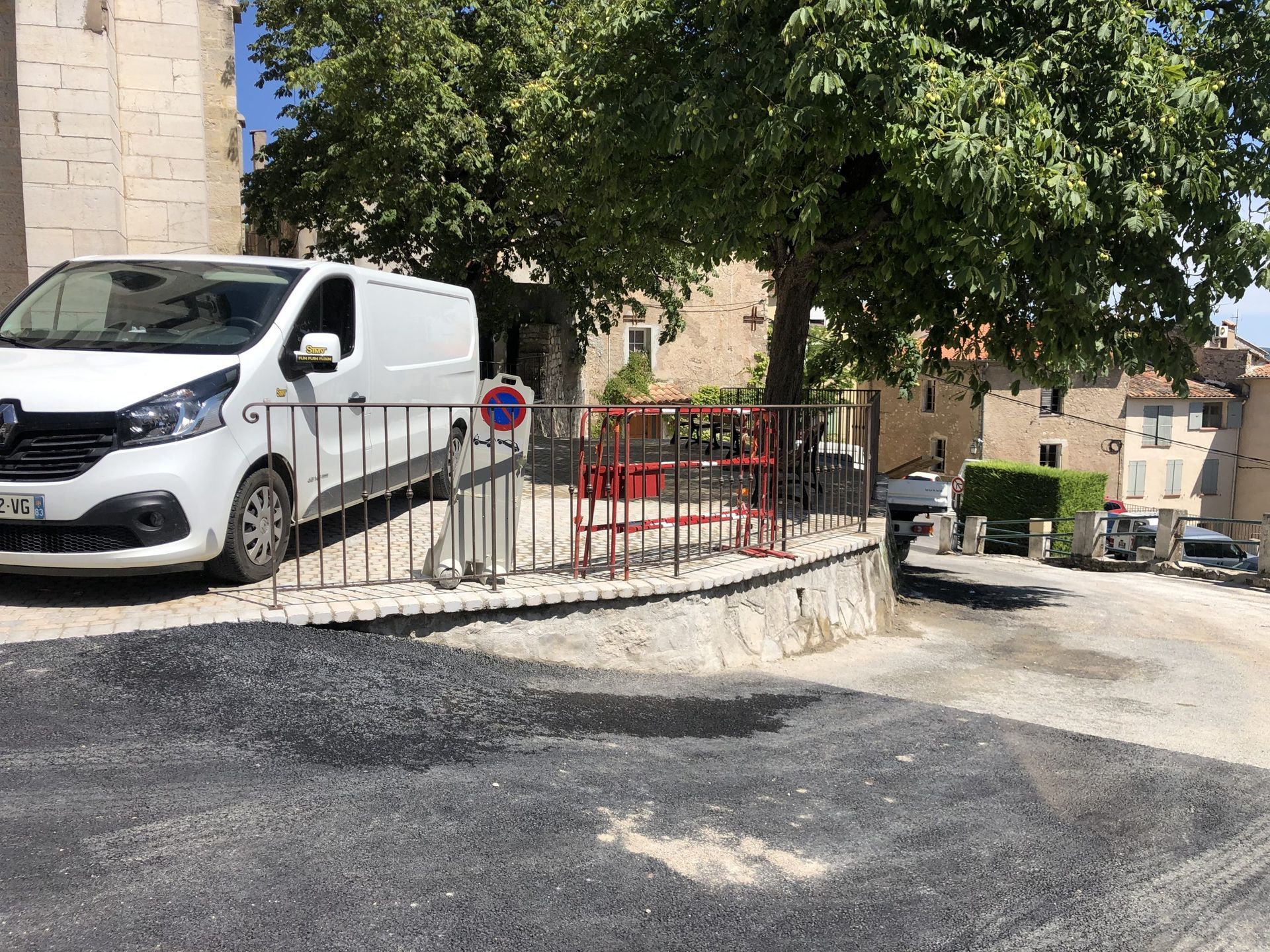 Fourgonnette avec porte latérale ouverte garée à côté d'un bâtiment en pierre et d'une cour arborée et clôturée.