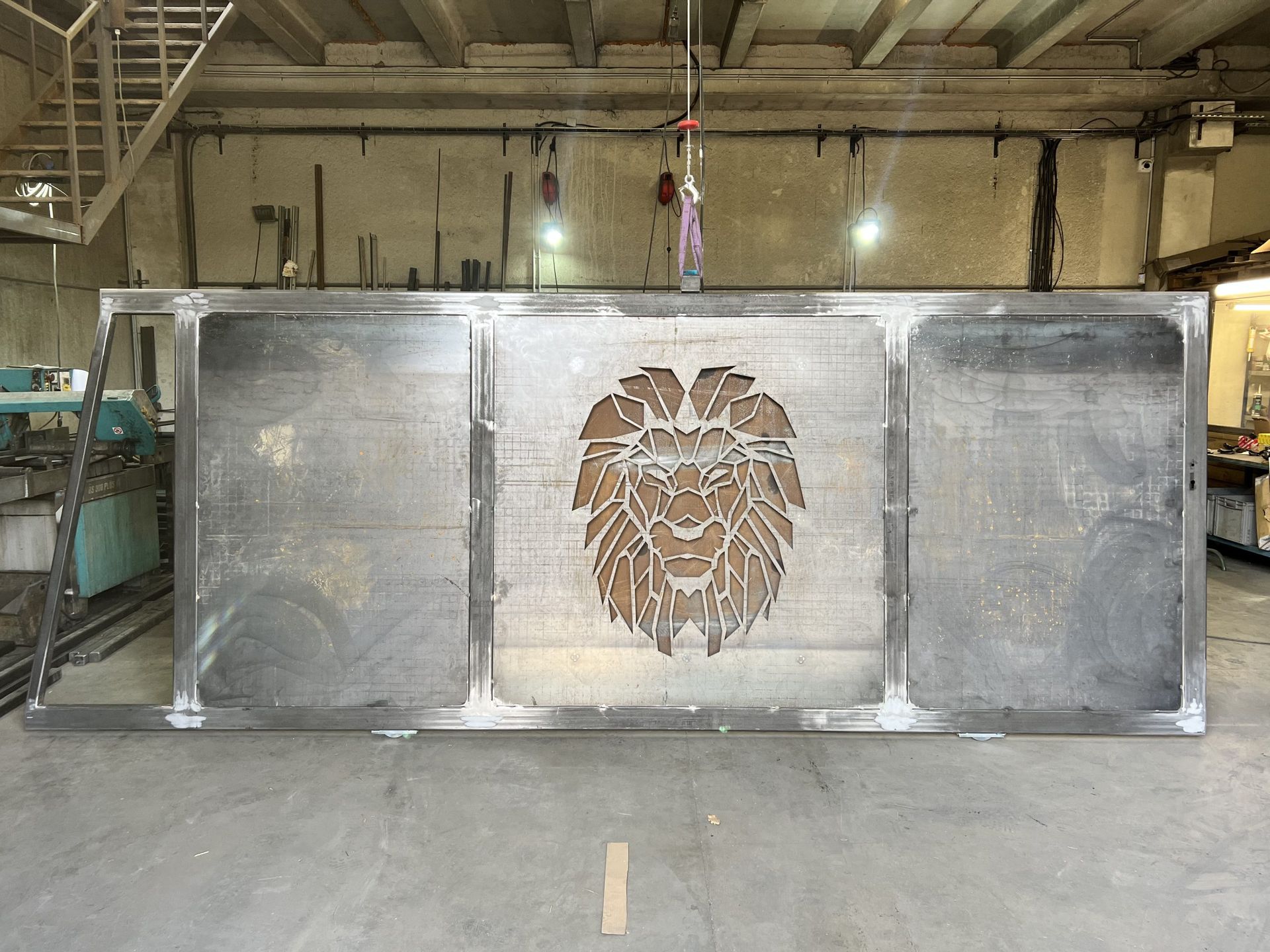 Grand panneau métallique orné d'un emblème en forme de tête de lion sculptée, dans un atelier industriel.