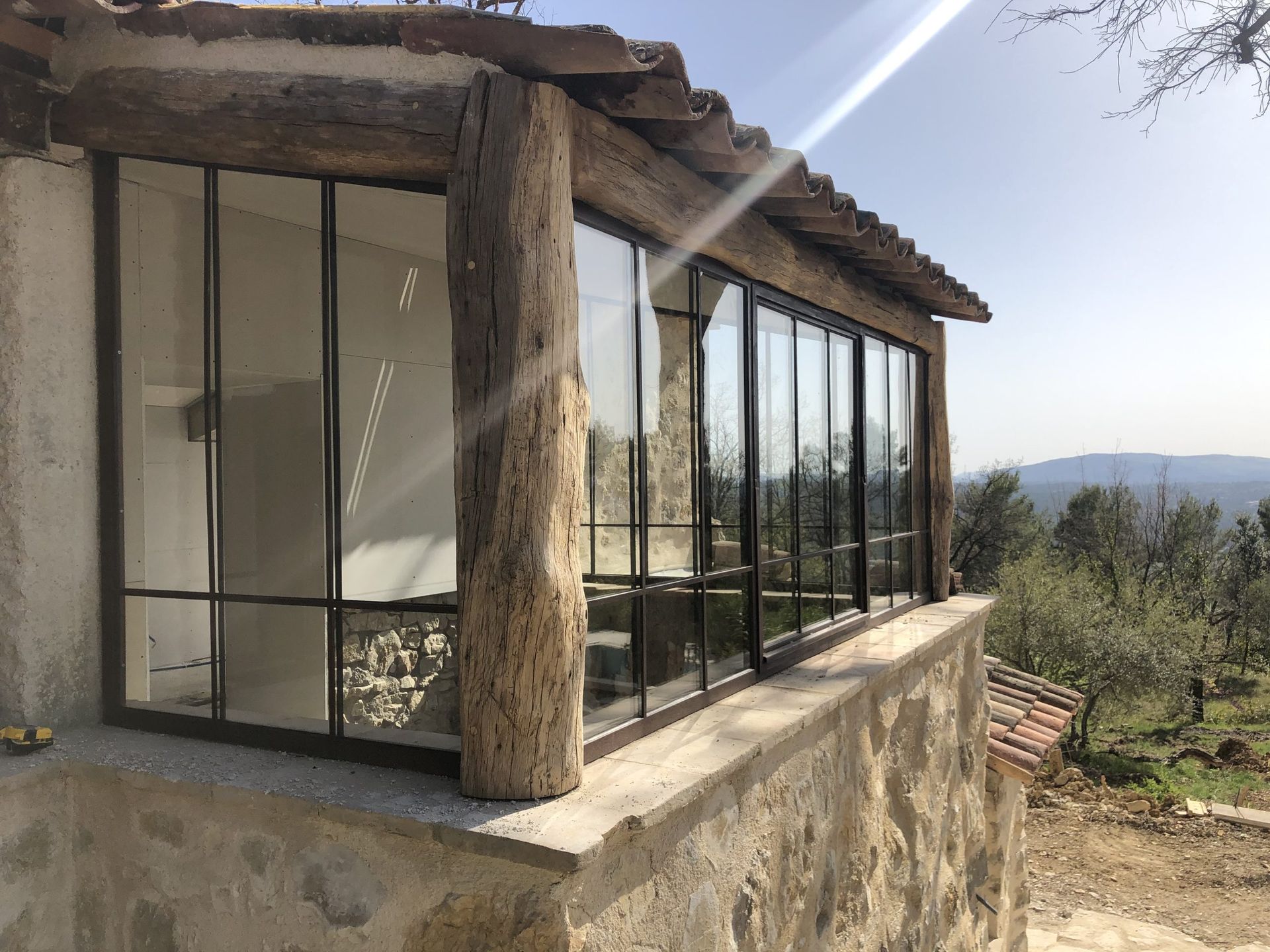 Maison en pierre avec des baies vitrées du sol au plafond donnant sur un paysage de colline ensoleillée
