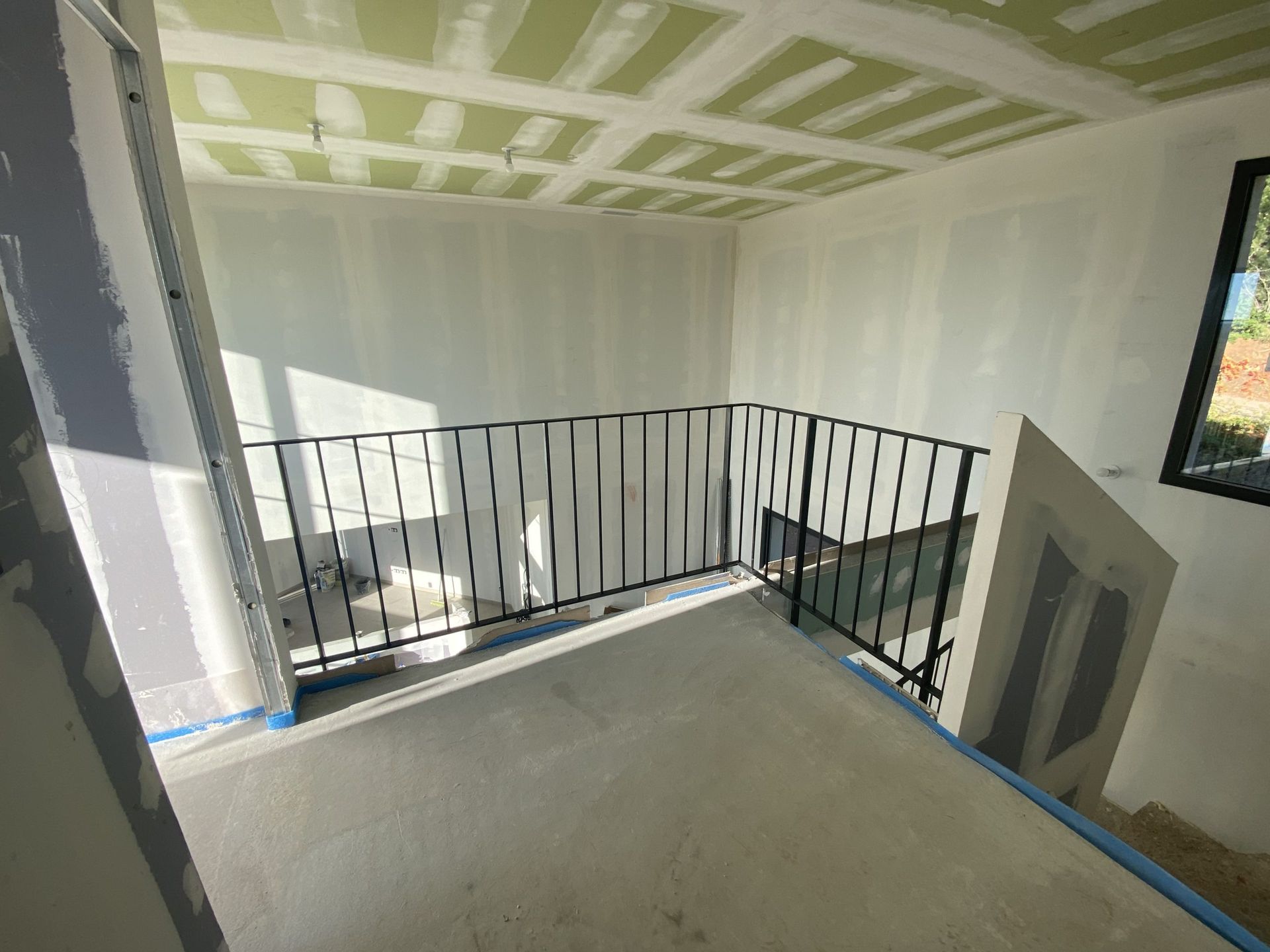 Palier d'escalier intérieur avec rampe en métal noir et sol en béton dans un espace partiellement aménagé
