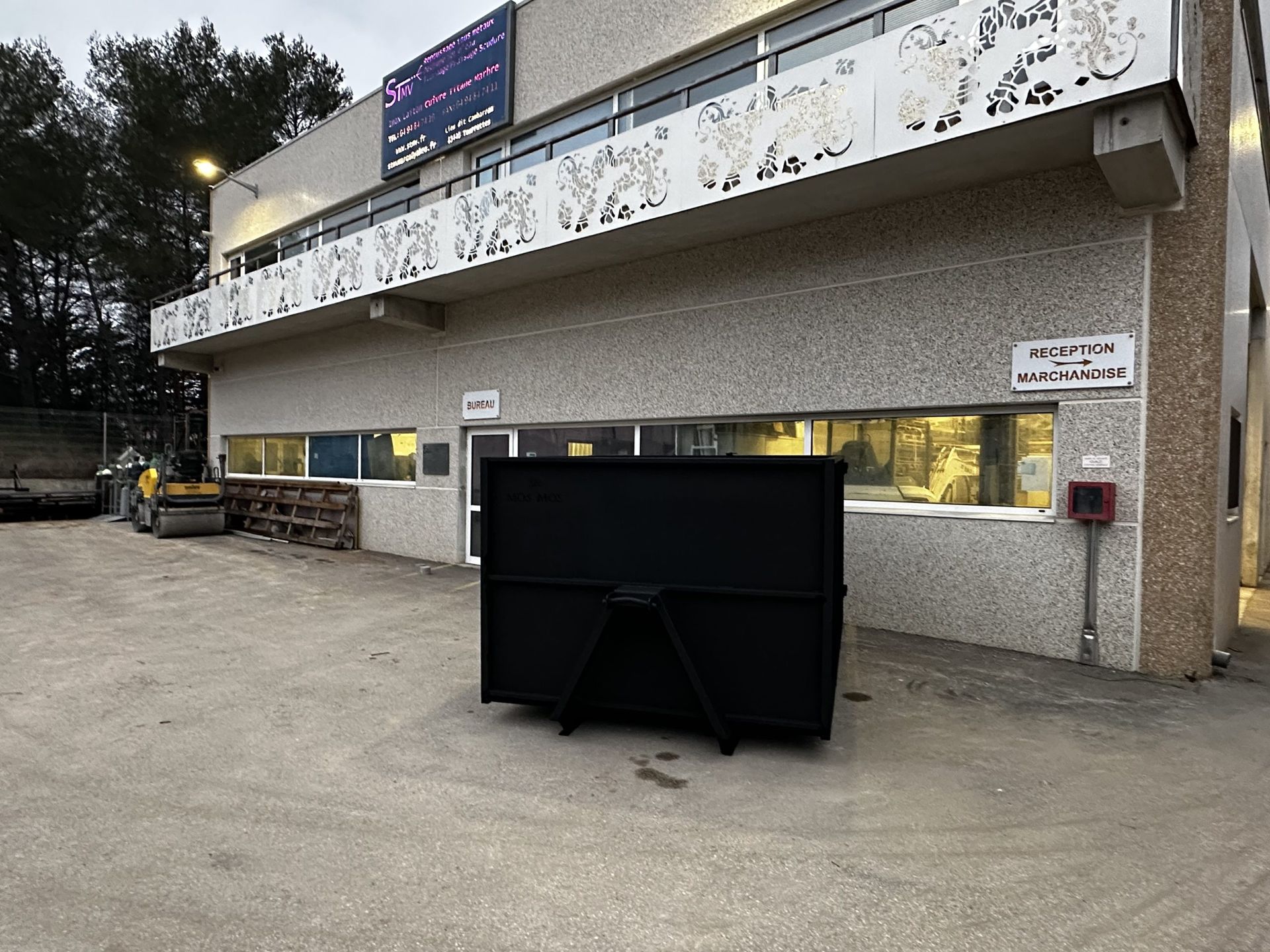 Bâtiment extérieur avec un grand écran numérique noir en façade et des fenêtres éclairées au crépuscule
