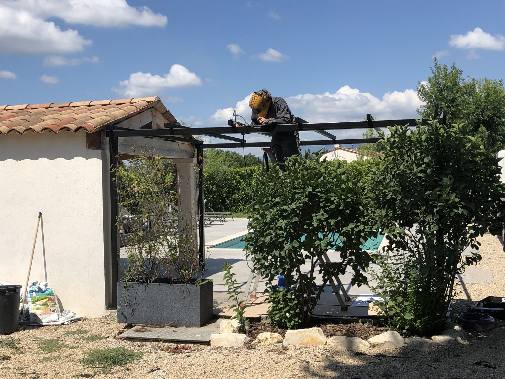 Petite pergola de jardin avec une statue de léopard, entourée de verdure à côté d'un bâtiment en stuc sous un ciel bleu.