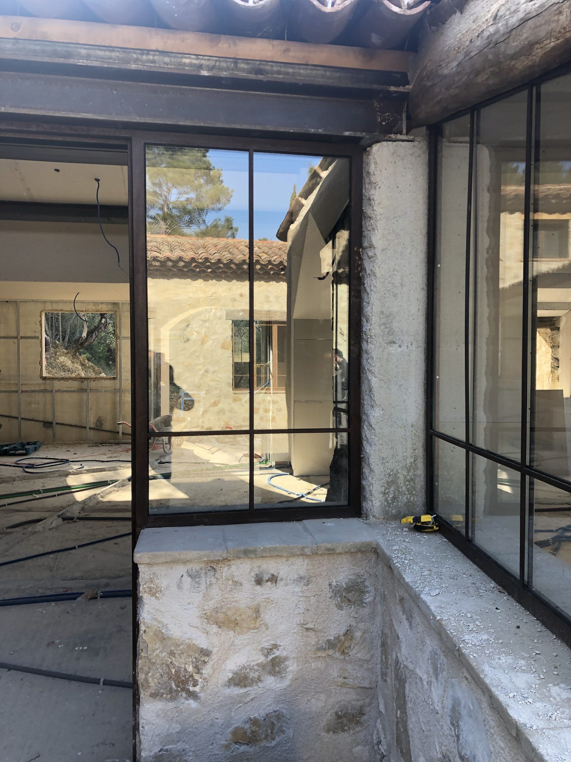 Patio abandonné avec béton fissuré, murs vitrés à cadre noir et vue sur une cour extérieure