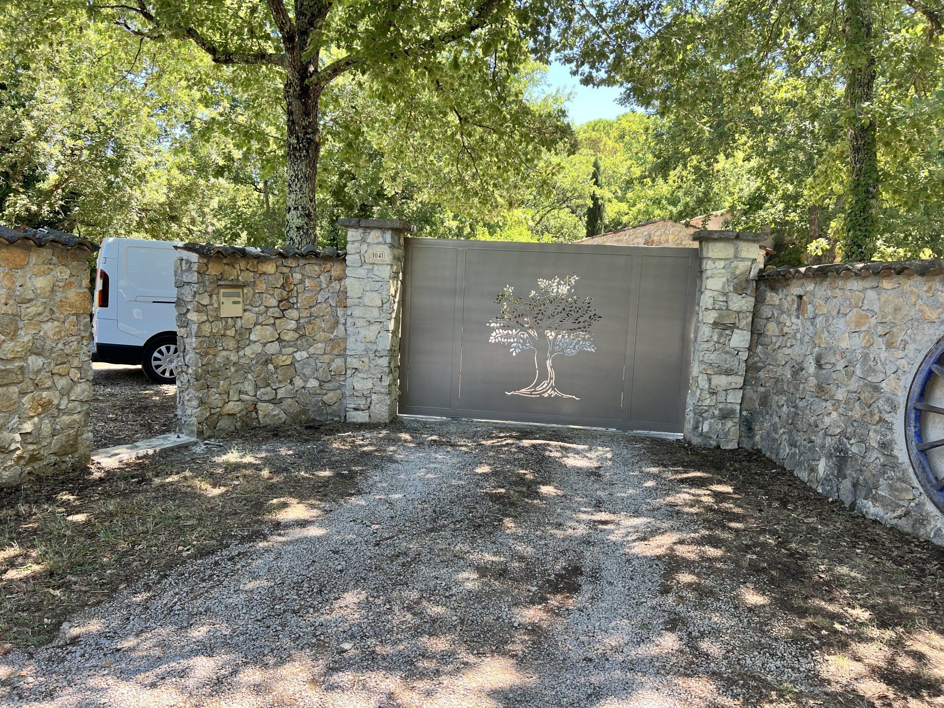 Mur de pierre et portail fermé le long d'une allée de gravier sous des arbres feuillus.