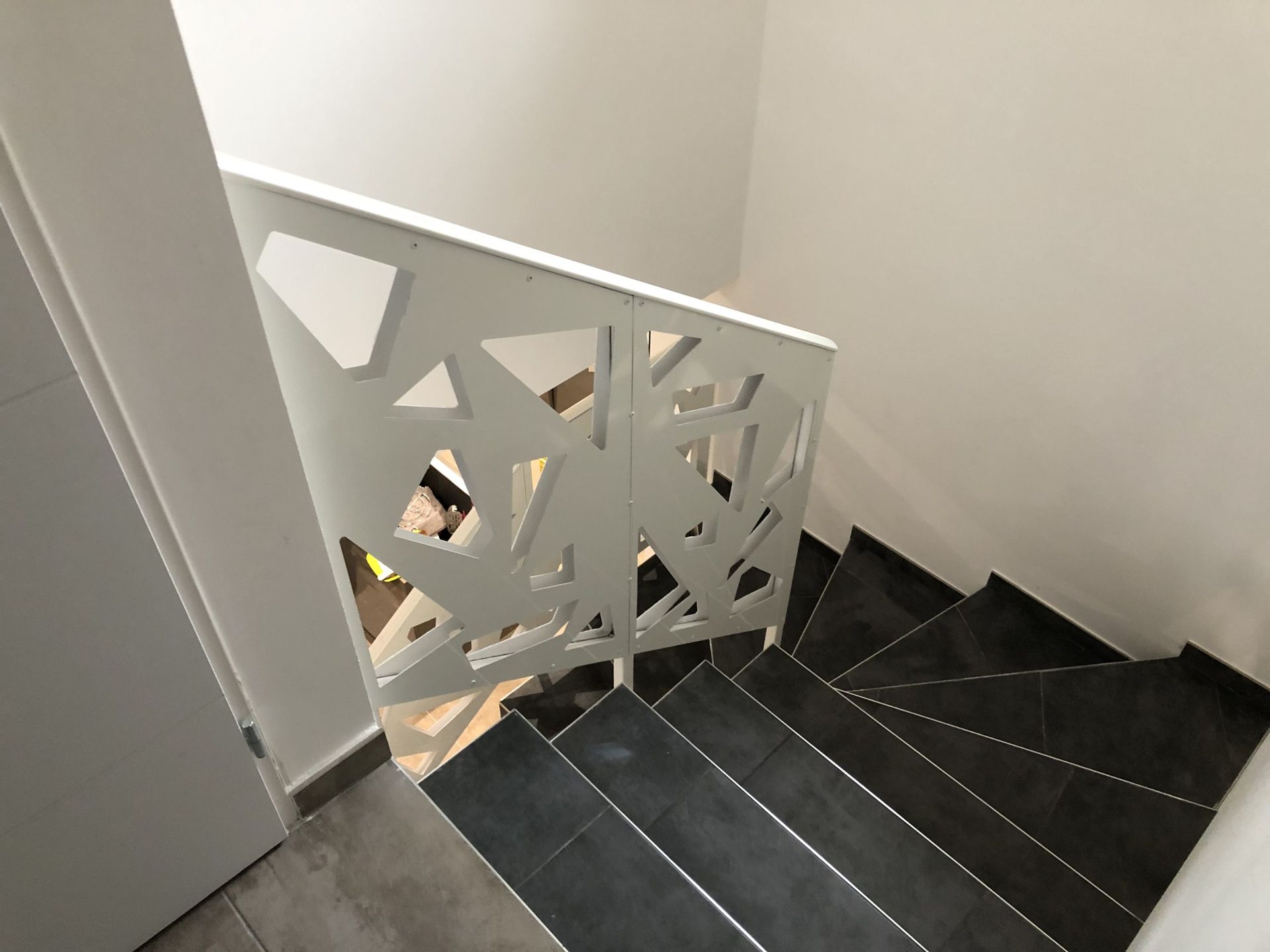 Escalier intérieur avec marches sombres et panneau de rampe géométrique blanc à côté d'une porte