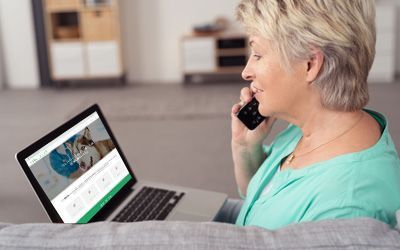 Una mujer está sentada en un sofá hablando por un teléfono celular mientras usa una computadora portátil.