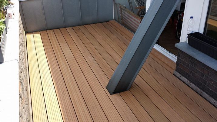 Holzterrasse mit hellbraunen Dielen und einem grauen Metallträger vor einer Glastür