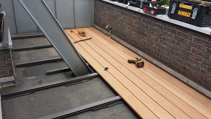 Bau einer Holzterrasse mit verlegten Dielen, sichtbaren Metallträgern und Werkzeugen wie Bohrmaschine und Schraubendreher.