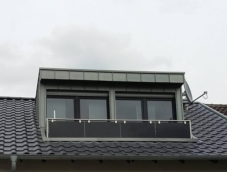 Gaubenfenster mit drei schwarzen Fenstern und schwarzem Geländer auf dunkelgrauem Ziegeldach