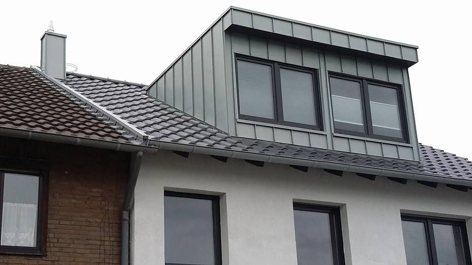 Dachgaube mit drei Fenstern auf einem Haus mit grauem Ziegeldach und weißer Fassade.