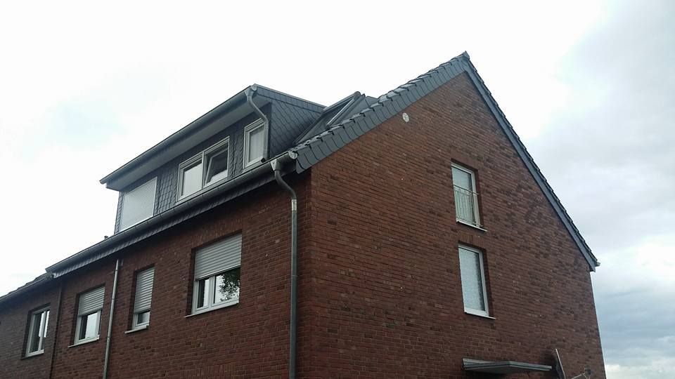 Zweistöckiges Wohnhaus aus rotem Backstein mit weißen Fensterrahmen und grauem Dach bei bewölktem Himmel.