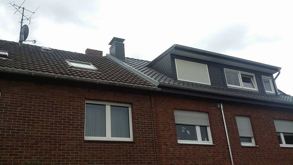 Zweistöckiges Backsteinhaus mit Dachfenster, Satellitenschüssel und geschlossenen Rollläden an bewölktem Himmel.