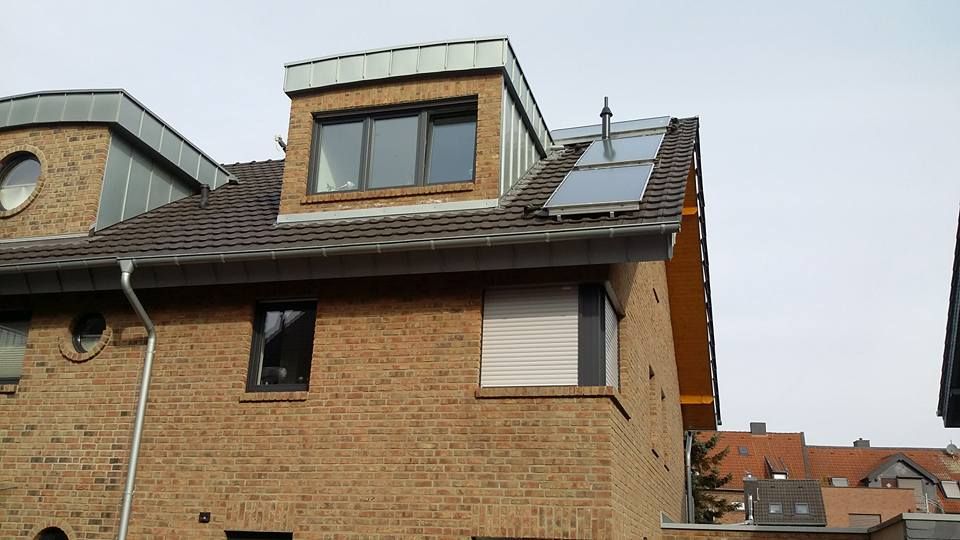 Backsteinhaus mit zwei Fenstern, einem runden Fenster, Dachfenster und Solarpanel auf dem Schrägdach.