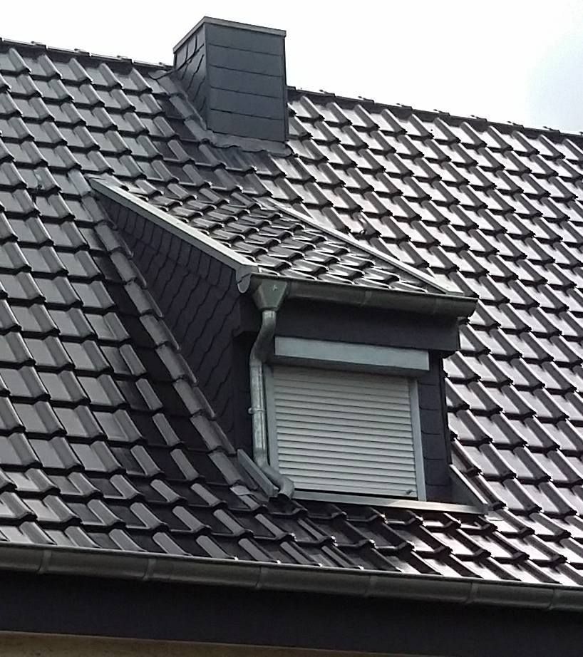 Dach mit schwarzen Ziegeln, Dachgaube mit geschlossenem Rollladen und Schornstein