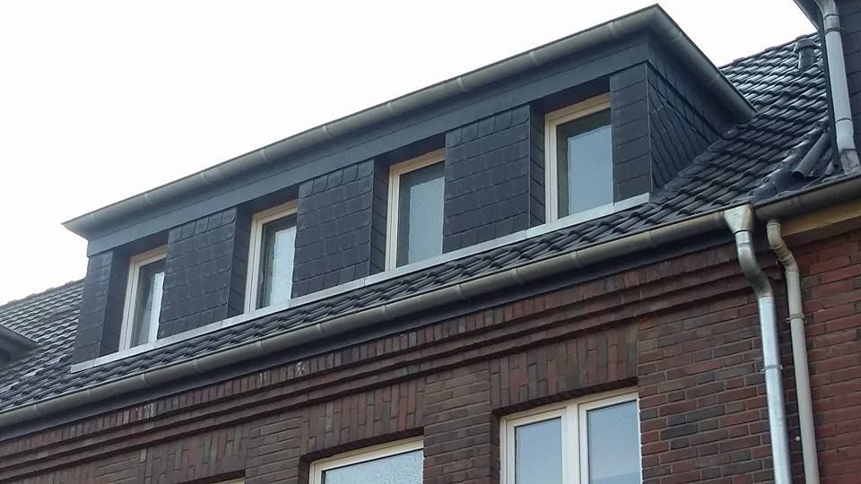 Fassade eines zweistöckigen Hauses mit dunkelgrauem Schieferdach und drei weißen Fenstern im Dachgeschoss.