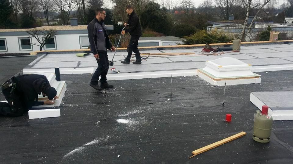 Dachdecker bei der Arbeit auf einem Flachdach mit Werkzeugen und Materialien.