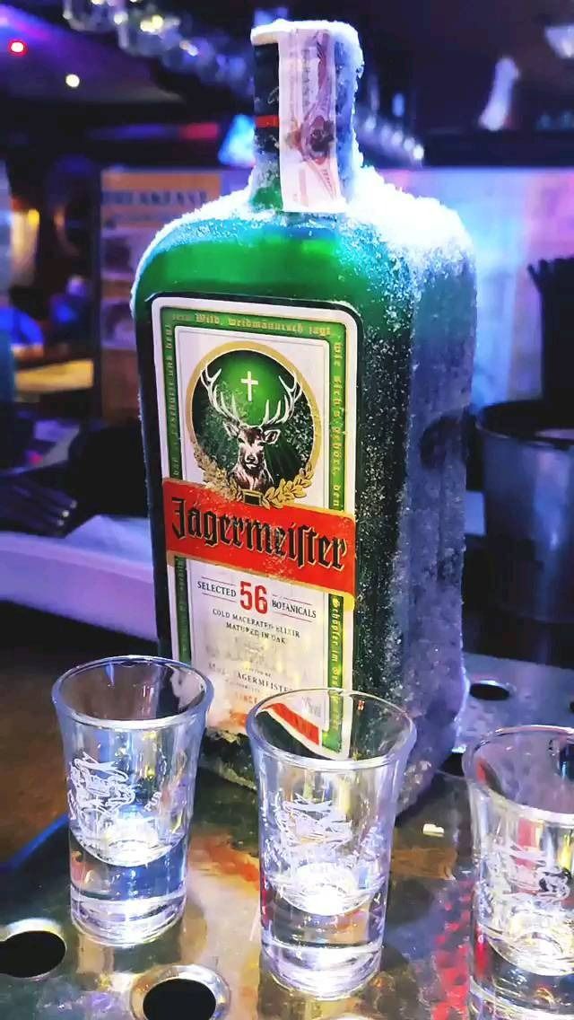 Una botella de Jägermeister está sobre una mesa al lado de tres vasos de chupito.