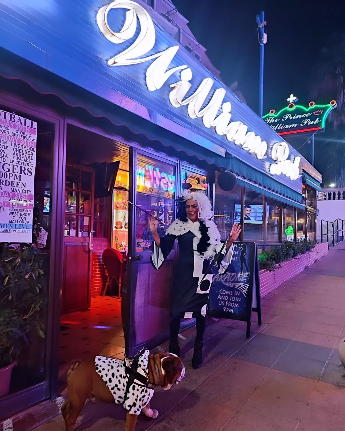 Una drag queen está parada junto a un perro frente a un restaurante.