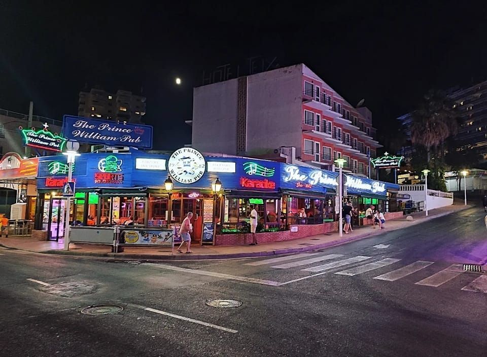 Un grupo de personas camina por una calle frente a un edificio por la noche.