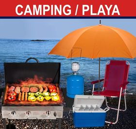 Montaje de camping en la playa con parrilla, sombrilla naranja, nevera portátil, linterna y silla roja junto al agua.