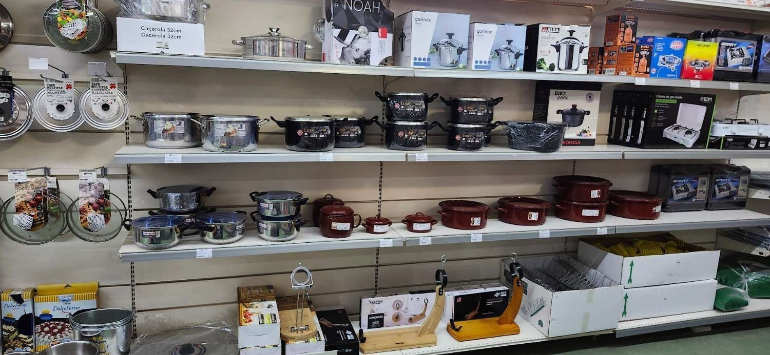Estantería de la tienda repleta de platos, utensilios de cocina y menaje variado en el pasillo de artículos para el hogar.