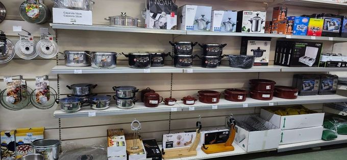 Estantería de la tienda repleta de platos, utensilios de cocina y menaje variado en el pasillo de artículos para el hogar.
