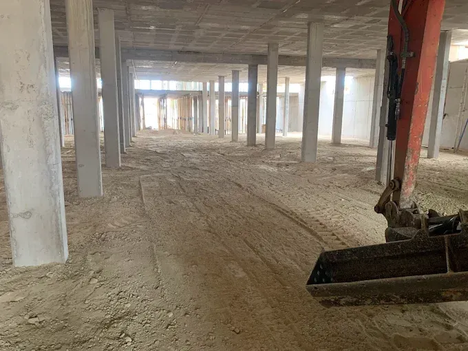 Una obra en construcción con varios pilares de hormigón y la pala de una excavadora en primer plano.