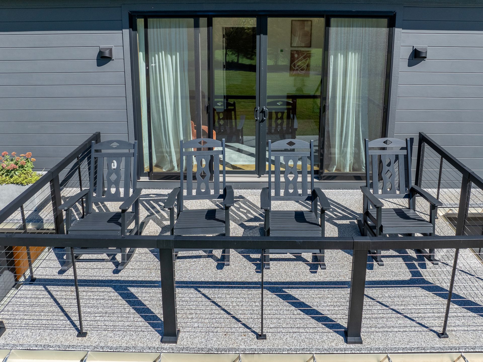 A patio with rocking chairs and a table in front of a house on the balcony facing the mountains.