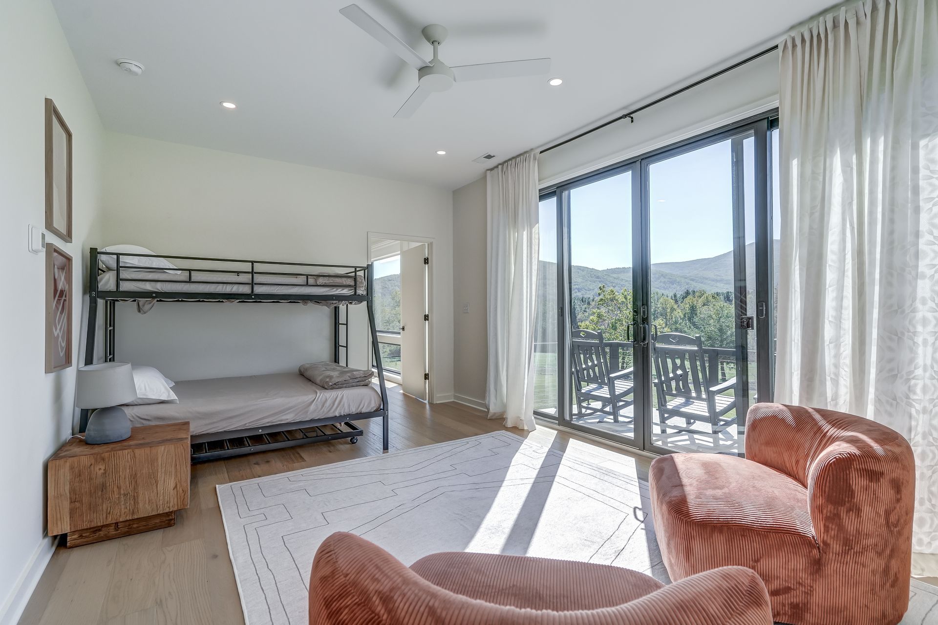 A bedroom with a bunk bed , chairs , and sliding glass doors.