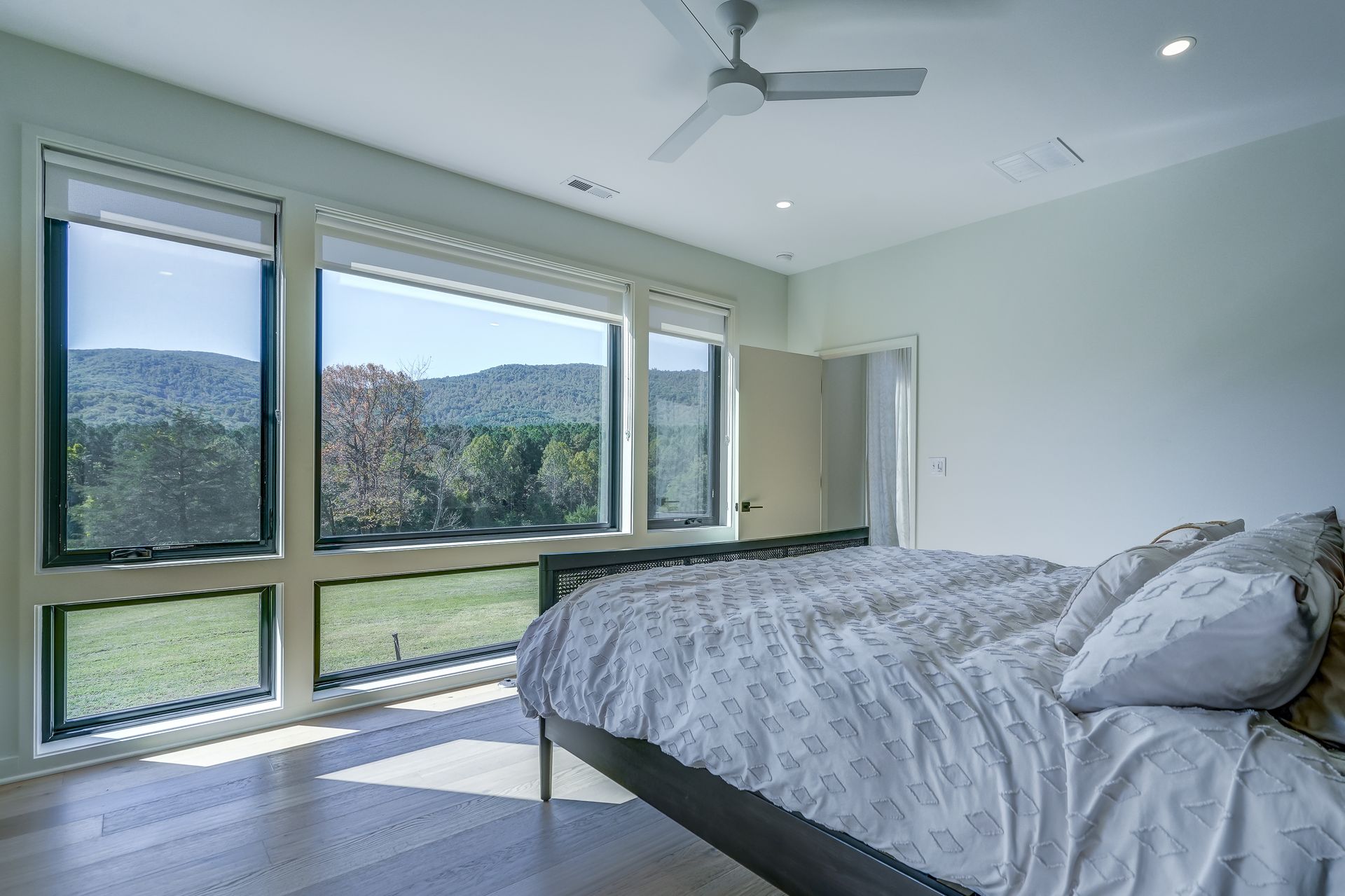 A bedroom with a bed , ceiling fan , and lots of windows.