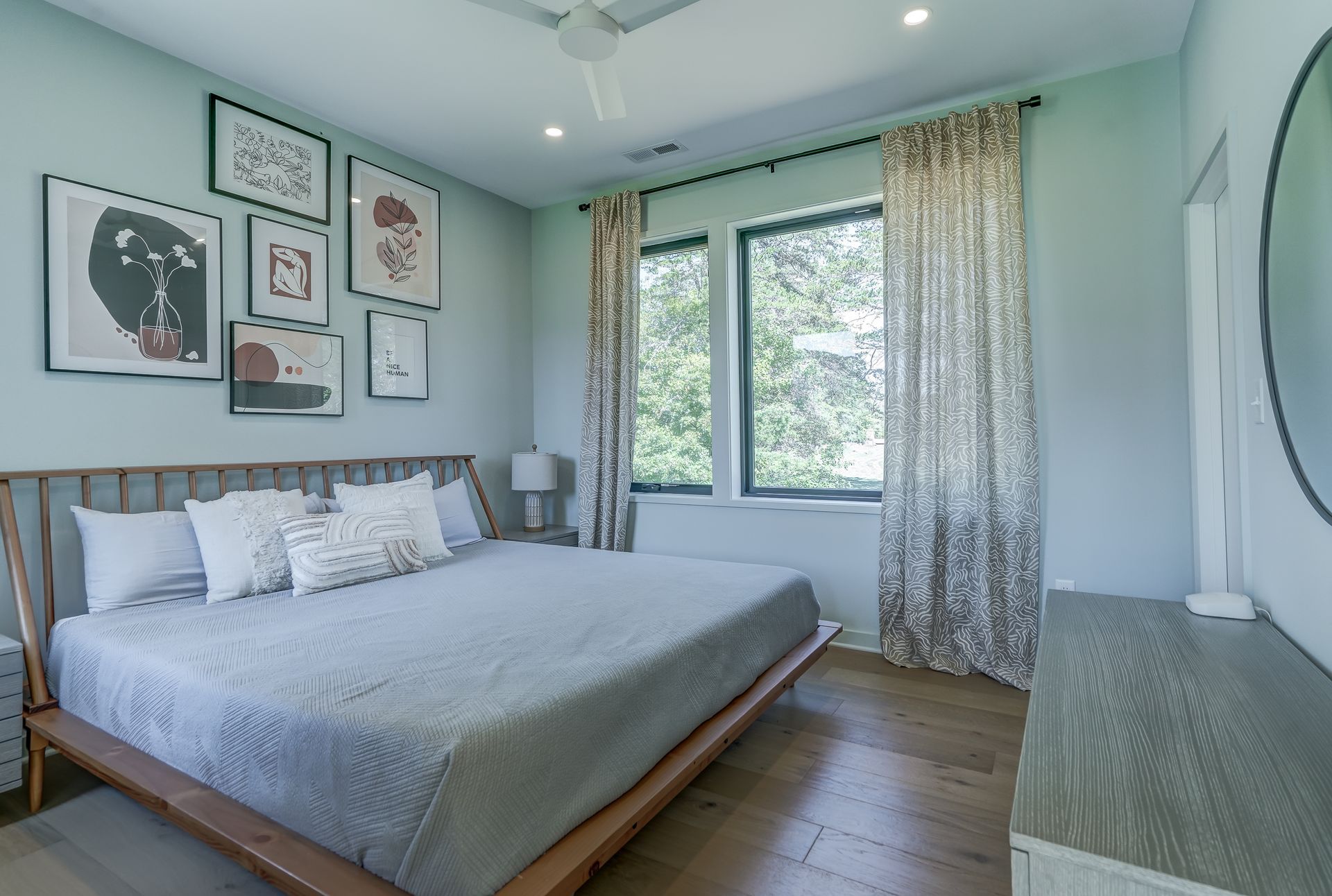 A bedroom with a king size bed , dresser , mirror and two windows.