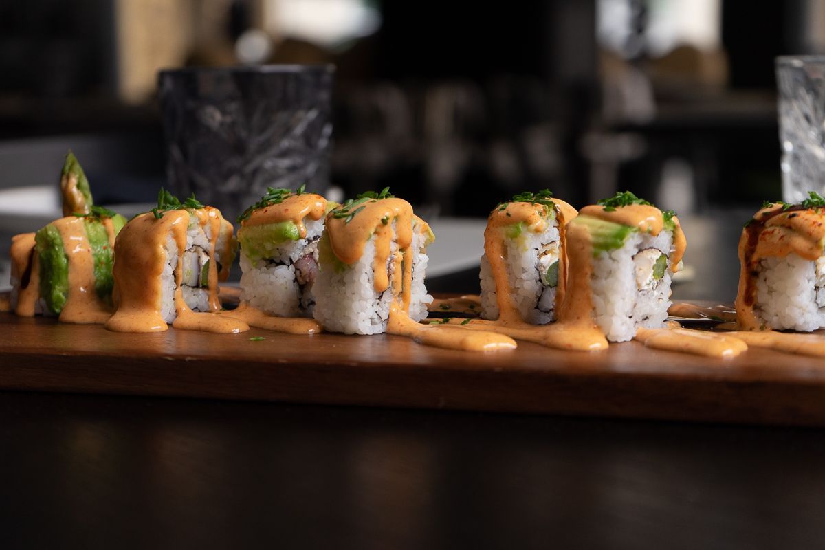 Una fila de rollos de sushi cubiertos de salsa sobre una tabla de cortar de madera.