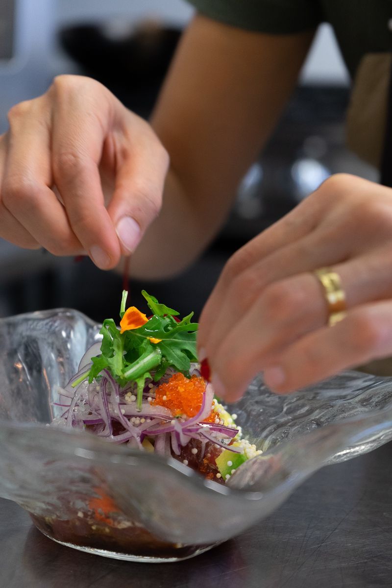Una persona está preparando una ensalada en un recipiente de vidrio.