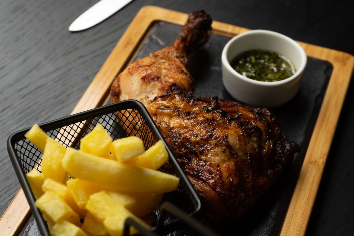 Hay una canasta de papas fritas al lado de un trozo de pollo en una tabla de cortar.