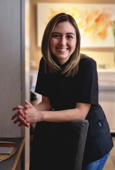 Una mujer con una camisa negra está sentada en una silla y sonriendo.