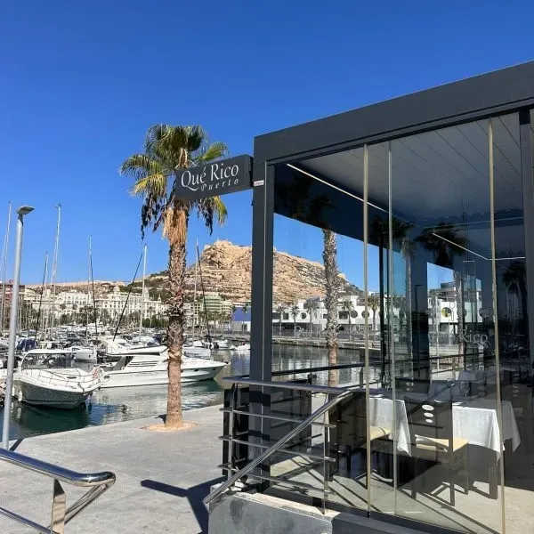 Mesa de playa preparada para comer con copas de vino, platos y mantel naranja con vistas al océano y a las palmeras.