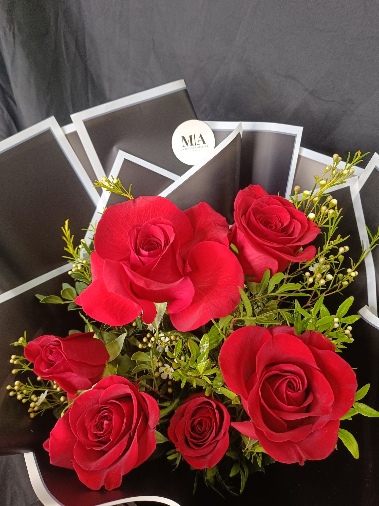 Ramo de rosas rojas con acentos verdes, envuelto en papel negro.
