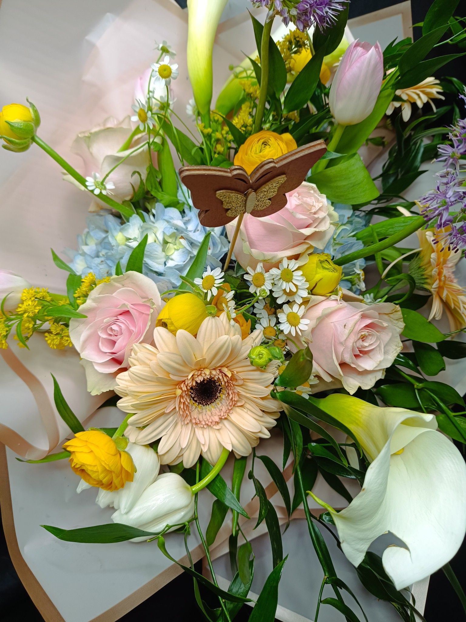 Ramo de rosas rosas y melocotón, margaritas gerberas, flores amarillas, lirios de cala blancos y un adorno de mariposa.
