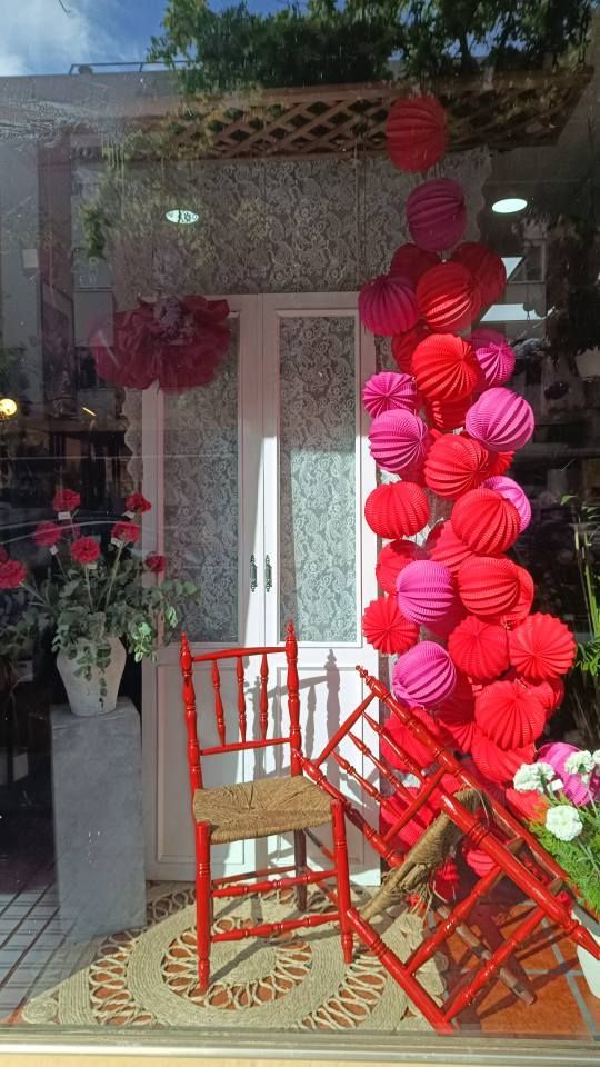 Escaparate con faroles de papel rojos y rosas, sillas rojas y flores.