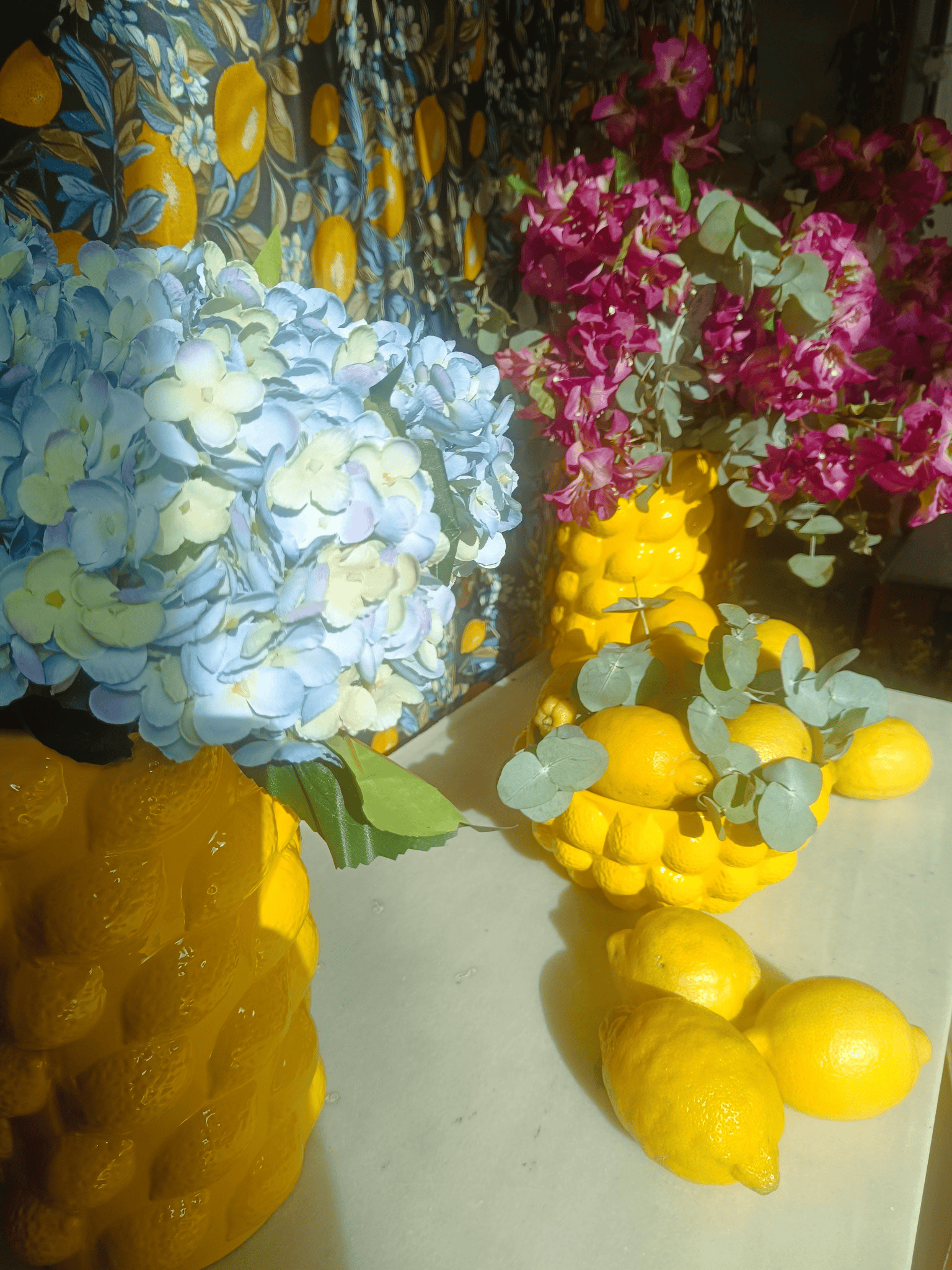 Limones y flores, incluidas hortensias azules y buganvillas moradas, sobre una mesa.