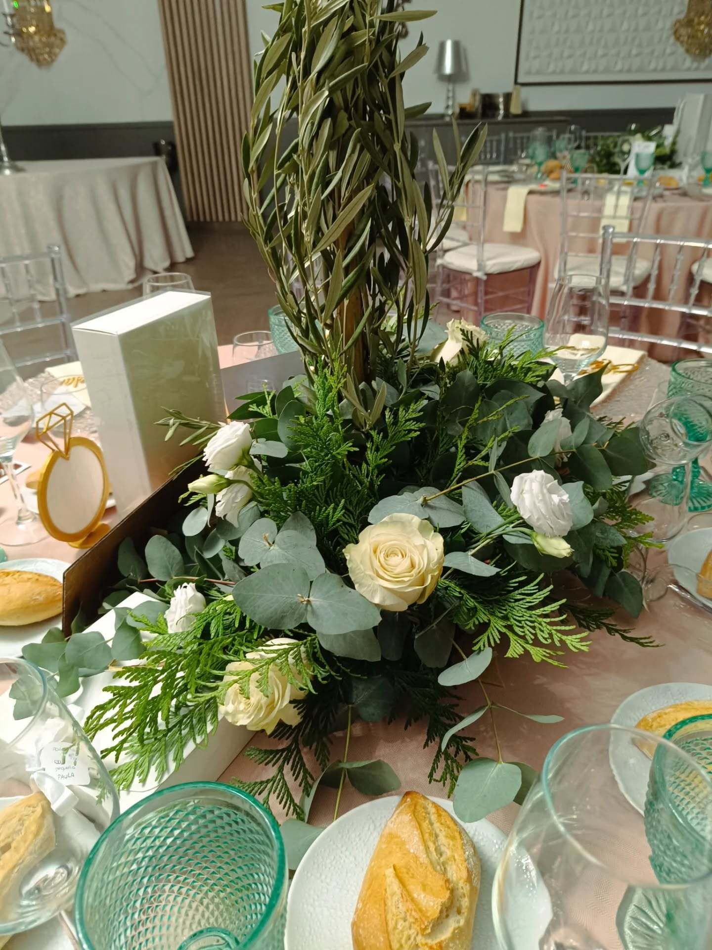 Centro de mesa floral sobre mesa preparada para evento formal con flores blancas, vegetación y una hogaza de pan.