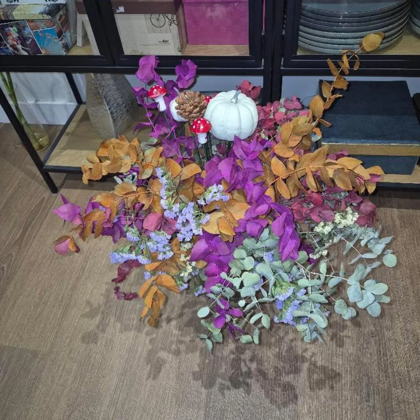 Arreglo floral artificial colorido con una calabaza blanca en el suelo de una tienda cerca de estantes negros.
