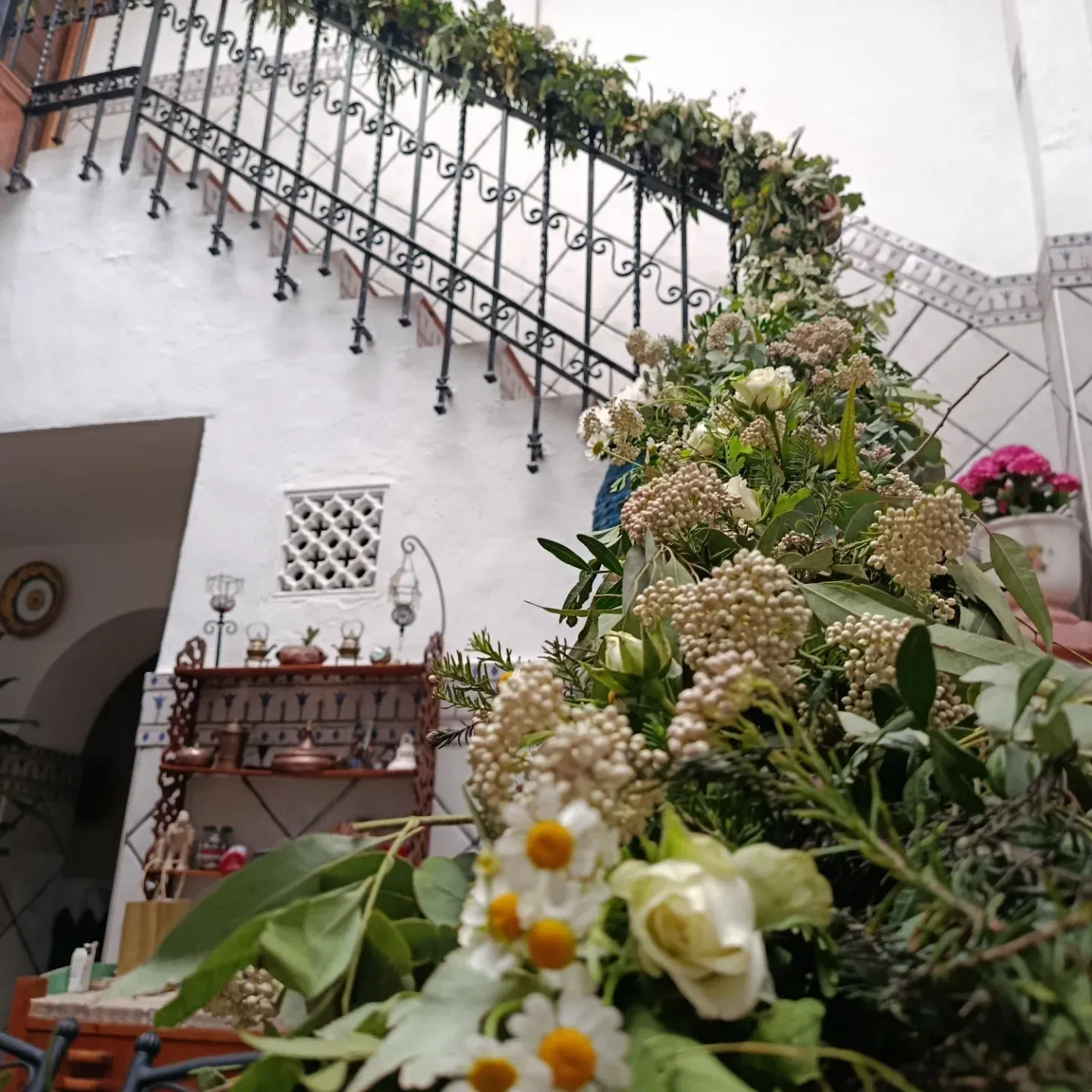 Patio blanco brillante con barandilla de escalera, estante de pared y un gran ramo de flores en primer plano.