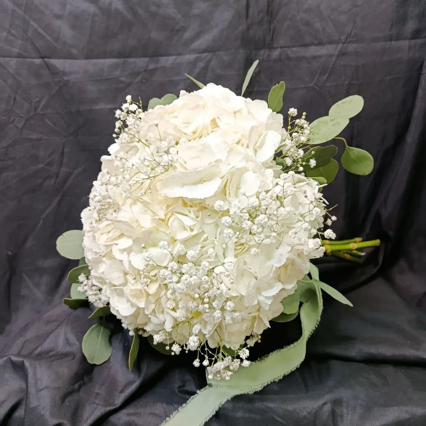 Ramo de hortensias blancas con paniculata y follaje sobre un fondo de tela oscura.