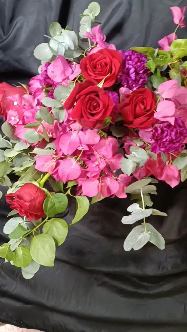 Ramo de rosas rojas, buganvillas rosas, claveles morados y eucaliptos verdes sobre fondo negro.