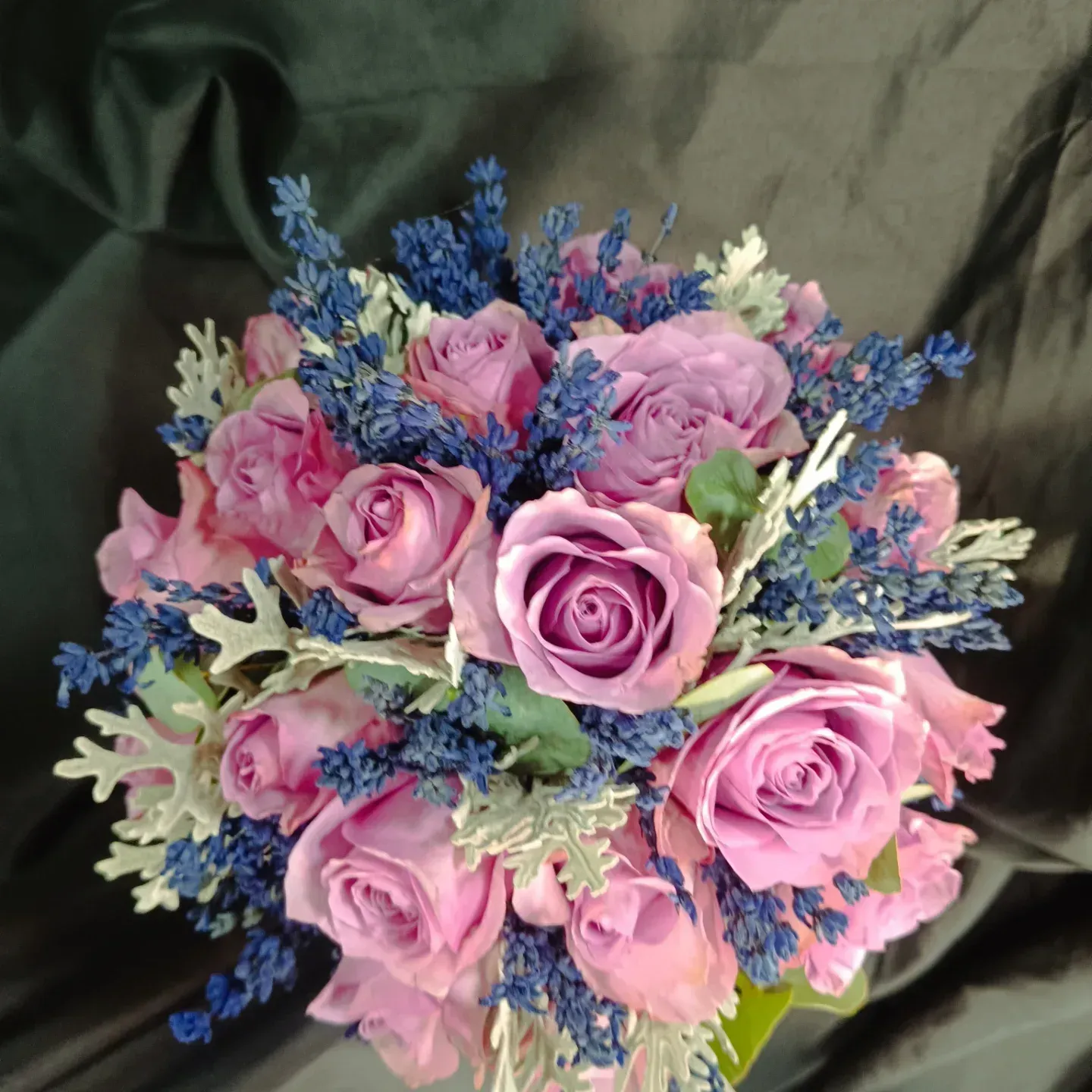 Ramo de rosas rosadas, lavanda azul y follaje plateado sobre un fondo oscuro.