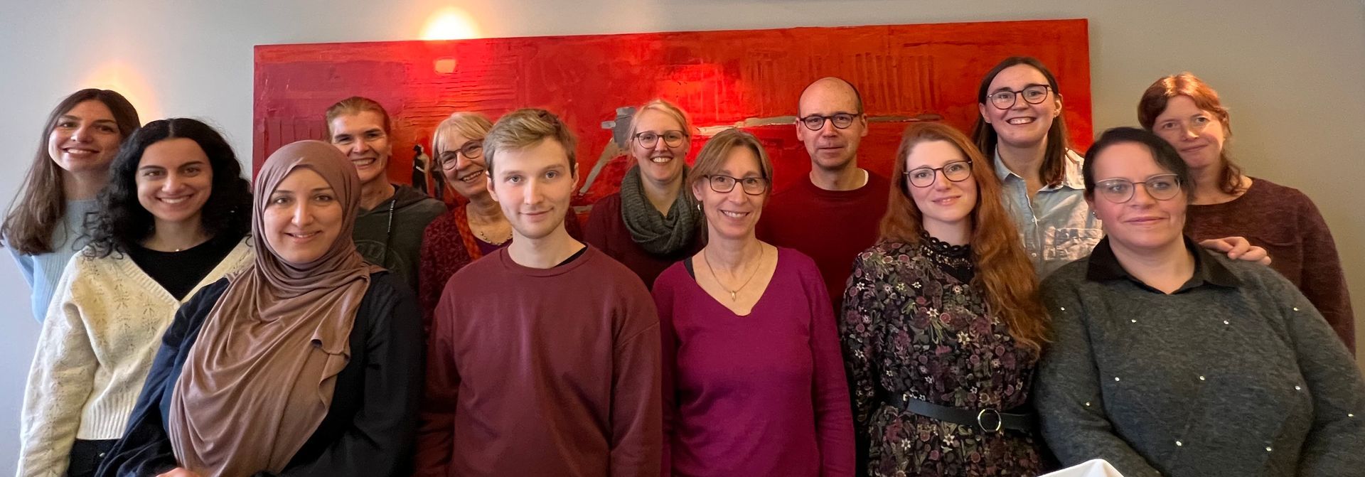 Das Team vom Kindertherapie-Zentrum Essen Steele vor einem roten abstrakten Gemälde in der Praxis.