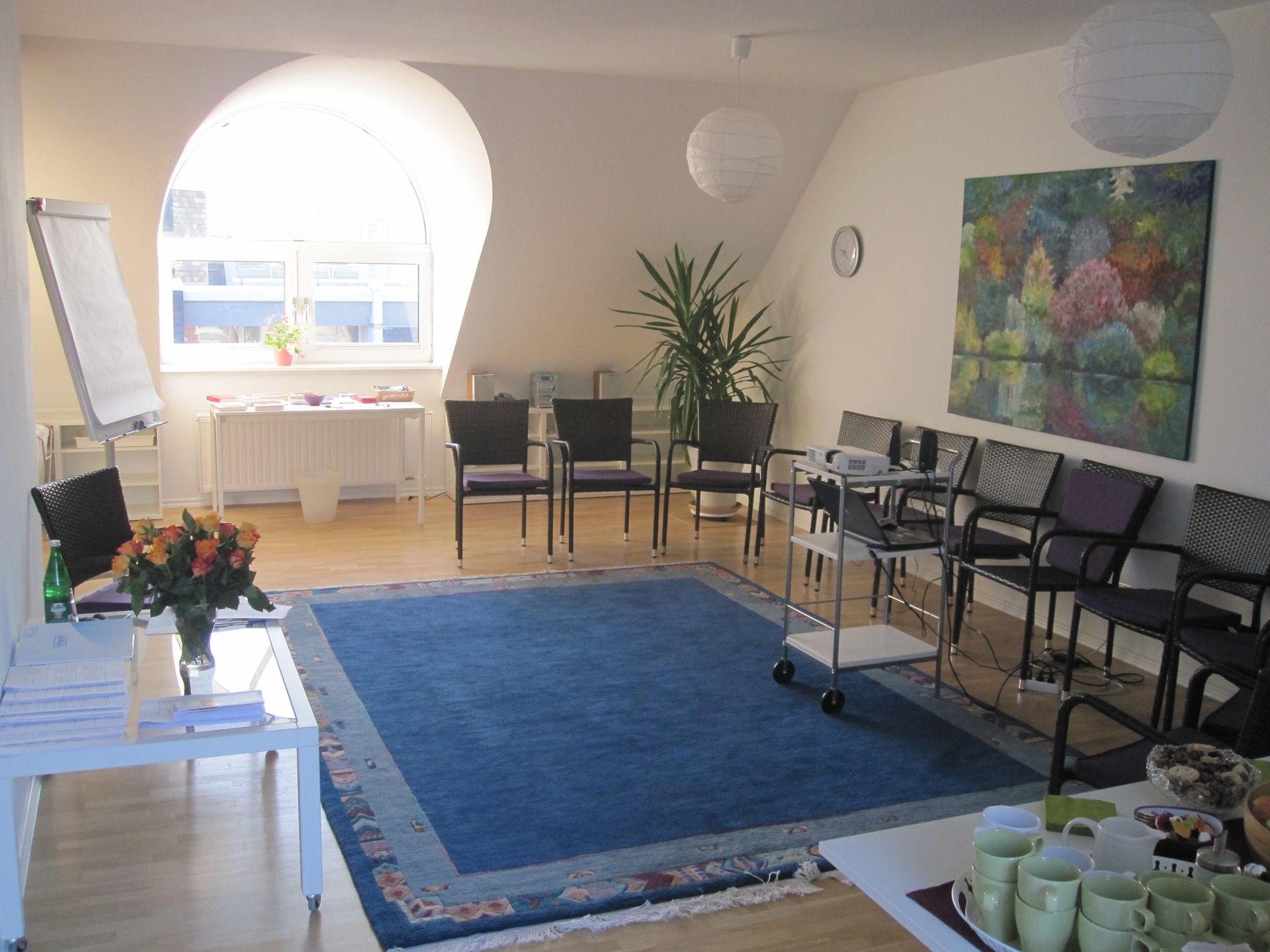 Besprechungsraum mit blauem Teppich, Stühlen, Flipchart und Kunstwerken. Das Fenster sorgt für Tageslicht.