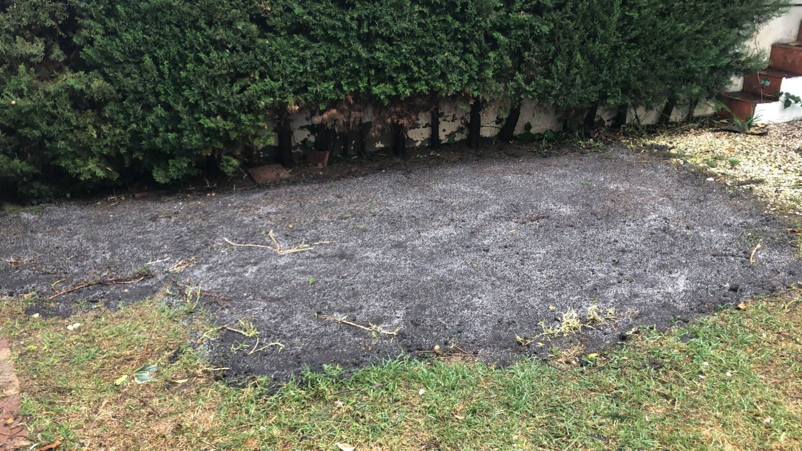 Mantillo oscuro delante de un seto verde y una pared de ladrillos, rodeado de césped.