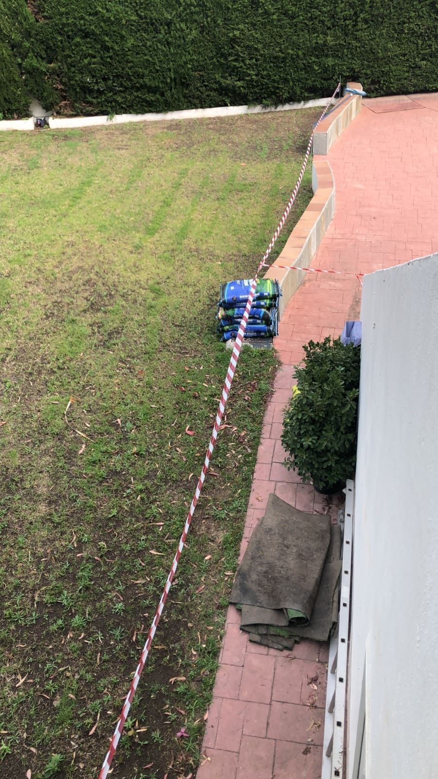 Un patio cubierto de césped con una pila de contenedores de almacenamiento azules, un camino de ladrillos rojos y cinta de seguridad.